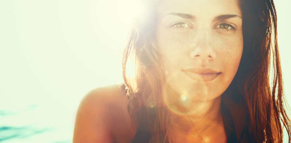 Ob durch die Sonne oder Selbstbräuner - eine junge Frau mit schön gebräunter Haut lächelt im Sonnenschein in die Kamera